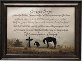 A framed wall art print featuring the text 'Cowboy's Prayer' in script and block lettering over a sepia-toned western landscape with a cowboy kneeling beside a horse and a cross. The piece is enclosed in a dark rustic wood frame.